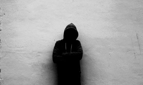 A hooded figure against a wall, image in black and white