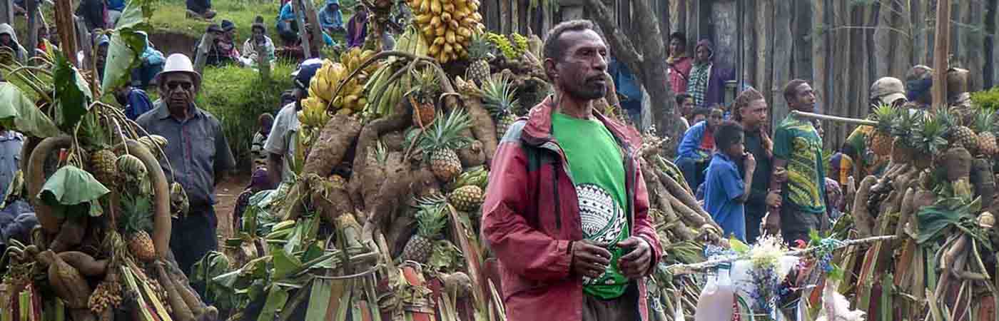 Person looking off to side of camera with pile of fruit and queue of people in the background